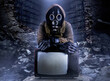 Photo of stalker soldier in jacket and armored vest and rubber gloves standing with old tv set on ruined dark background.