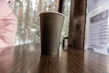 A Black Paper Cup Of Coffee Stands On A Bar Counter In A Cafe Overlooking The Snowy Winter