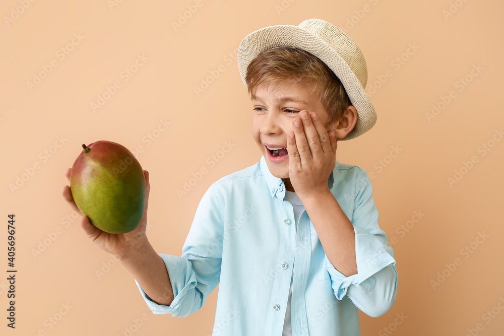 Cute little boy with fresh tasty mango on color background
