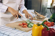 © wutzkoh - Woman using knife and hands cutting cucumber on wooden board in kitchen room.