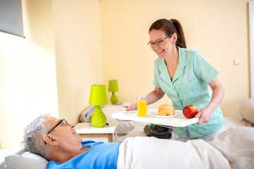 Nurse in a old people’s home providing residential care by bringing breakfast to her senior man occupant