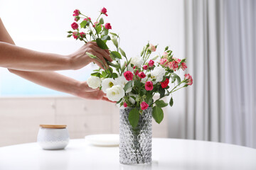 Wall Mural - Woman taking beautiful flowers from vase on white table in room, closeup