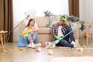 Canvas Print - Tired couple sitting in messy room while cleaning after New Year party