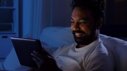 Sticker - technology, internet, communication and people concept - young indian man with tablet pc computer lying in bed at home at night