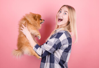 Canvas Print - A cute young woman is holding her Pomeranian puppy. Love between owner and dog. Isolated over pink background. Studio portrait.