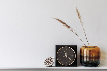 Minimalistic composition on the wooden shelf with dried flowers in vase and elegant personal accessories in stylish living room interior. Copy space.