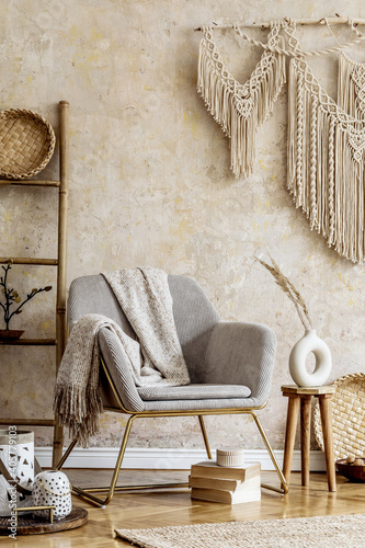 Obraz Dibond Stylish oriental living room with design armchair, beautiful macrame, wooden ladder, plant, decoration, carpet, coffee table, book and elegant personal accessories in wabi sabi concept.