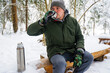 a guy in a winter forest drinks a hot drink from a thermos bottle, a tourism concept