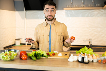 Young guy is curious about cooking vegetarian food. Handsome man doesn't know what to cook using only vegetables because he try to be vegan