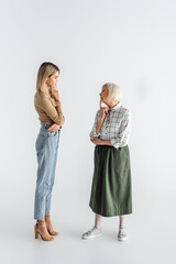 Sticker - full length of thoughtful granddaughter and senior granny standing and looking at each other on white