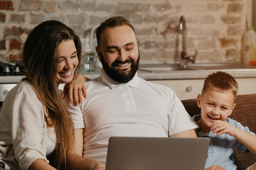 A close up photo of the happy family. A smiling father is working remotely on a laptop while his son and wife are staring at the screen. Dad is working online on a computer with relatives at home