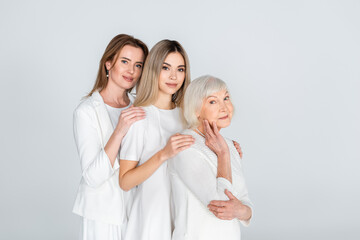 Sticker - three generation of joyful women smiling while looking at camera and hugging isolated on grey