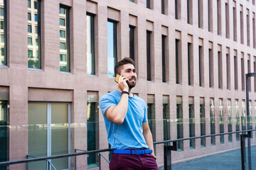 Portrait of cheerful modern businessman speaking by phone and smiling while standing outdoors