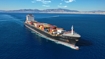 Aerial drone photo of industrial colourful vessel carrying heavy truck size containers cruising the Aegean deep blue sea