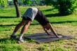 © qunica.com - Young caucasian man practicing yoga on a mat outdoors at the park in downward facing dog pose