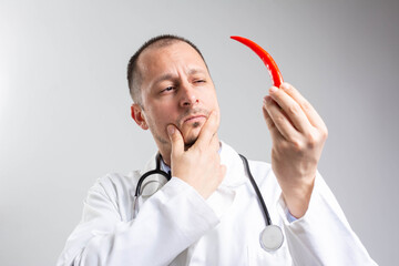 Handsome doctor in a white coat holding red hot chili pepper and thinking about Health Benefits of Capsaicin.