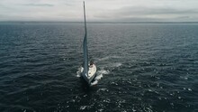 Aerial View. A White Sailing Yacht Changes Course. The Boat Maneuvers In The Sea At Full Speed. The Sailboat Makes A Tack Turn. Yachting On Windy And Sunny Day At Sea. Drone Shot.