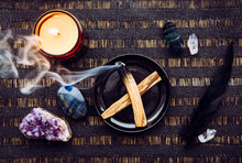 Flat Lay View Of Palo Santo Wood Known As Oily Aromatic Holy Wood Sticks Smouldering On Plate On Home Table Cleaning Negative Energy Concept. Surrounded With Gemstones Amethyst And Labradorite.