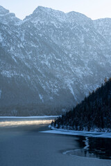 Wall Mural - Portrait format of frozen lake Plansee in winter with water vapor in the sunlight