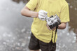 A boy in a yellow t-shirt and shorts is standing near the water in nature and washing a camera with soap and foam. The concept child is a bully. photographers day