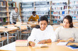 © JackF - Two hispanic women engaged in research, looking together for information in books in public library