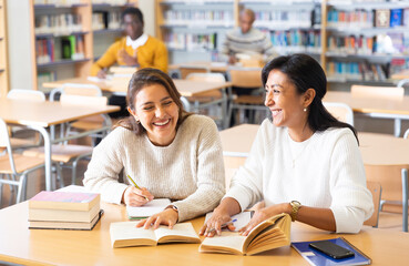 Two young adult women gaining new skills at public library, reading books and making notes