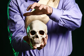 Male fortune teller with human skull on dark background, closeup