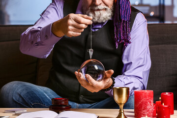 Wall Mural - Male fortune teller with crystal ball and pendulum at home