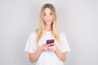 © Studio Nova - Excited young woman looking in surprise at camera holding mobile phone, smiling. Woman reading a text message on her phone, isolated on white background.