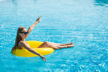 Wall Mural - Summer vacation. Beautiful slim young woman enjoying an aqua park floating in a yellow big ring on sparkling blue pool