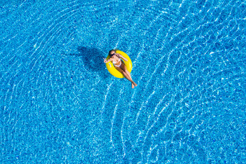 Wall Mural - Aerial view of young brunette woman swimming on the inflatable big donut in the transparent turquoise sea. Top view of slim lady relaxing on her holidays