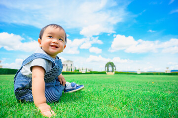 Boy among green grass s on a summer day. A small child has fun in the fresh air. Baby explores the nature with blue sky