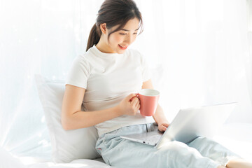 Wall Mural - Young Asian woman sitting on bed working watching home entertainment