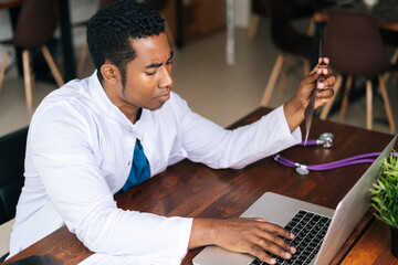 Poster - Top view of African American black male doctor in white coat analyzing history disease of patient using MRI brain head scan, working on laptop. Concept of medicine and health care.