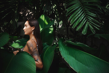 Sensual woman with summer tan and tattoo, wearing bikini and walking in jungles, posing with palm tropical leaves on summertimes vacation to paradise resort