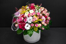 Floral Arrangement With Orchids, Cotton And Other Flowers In A Large Hat Box On A Dark Background.