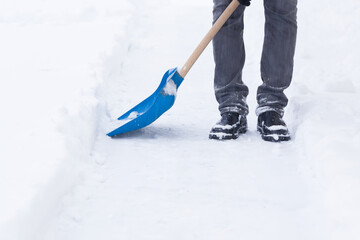 man shoveling fresh white snow with blue shovel on sidewalk after blizzard in winter day. closeup.