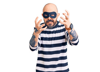 Wall Mural - Young handsome man wearing burglar mask shouting frustrated with rage, hands trying to strangle, yelling mad