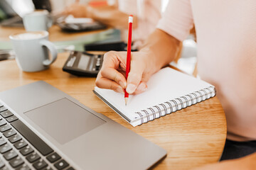 Man writes business information in notebook at workplace in office with calculator and laptop