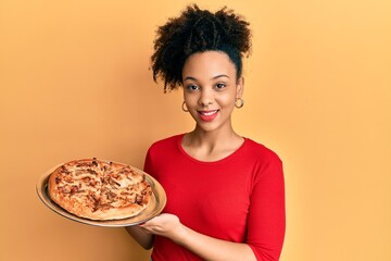 Poster - Young african american girl holding italian pizza looking positive and happy standing and smiling with a confident smile showing teeth