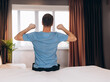 © Ivan - Good morning Young man waking up in bed and stretching his arms, back view, copy space.