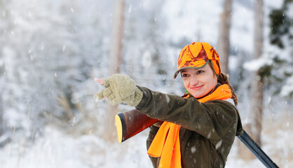 Wall Mural - A young beautiful hunter woman on hunt in forest with rifle on the shoulder. Winter season. In the background are snowy trees. Copy space for text.