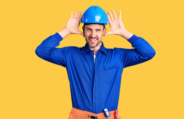 Sticker - Young handsome man wearing worker uniform and hardhat smiling cheerful playing peek a boo with hands showing face. surprised and exited