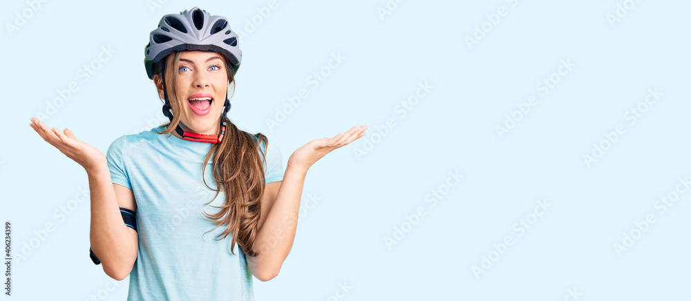 Beautiful caucasian young woman wearing bike helmet celebrating victory with happy smile and winner expression with raised hands - obrazy, fototapety, plakaty 