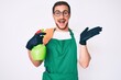 © Krakenimages.com - Young handsome man wearing apron holding sprayer celebrating victory with happy smile and winner expression with raised hands