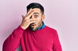 © Krakenimages.com - Young hispanic man wearing casual clothes peeking in shock covering face and eyes with hand, looking through fingers with embarrassed expression.