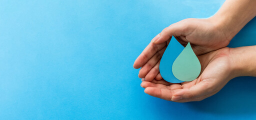 Woman hands holding paper cut water drop on blue background. Clean water and sanitation, saving water. World Water Day. Ecology concept.