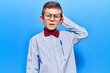 Cute blond kid wearing nerd bow tie and glasses confuse and wonder about question. uncertain with doubt, thinking with hand on head. pensive concept.
