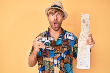 Poster - Young blond man holding vintage camera and city map afraid and shocked with surprise and amazed expression, fear and excited face.