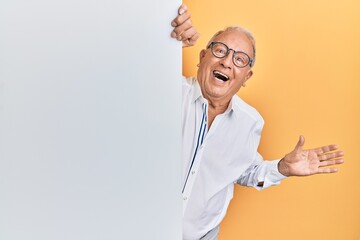 Senior caucasian man holding blank empty banner celebrating victory with happy smile and winner expression with raised hands